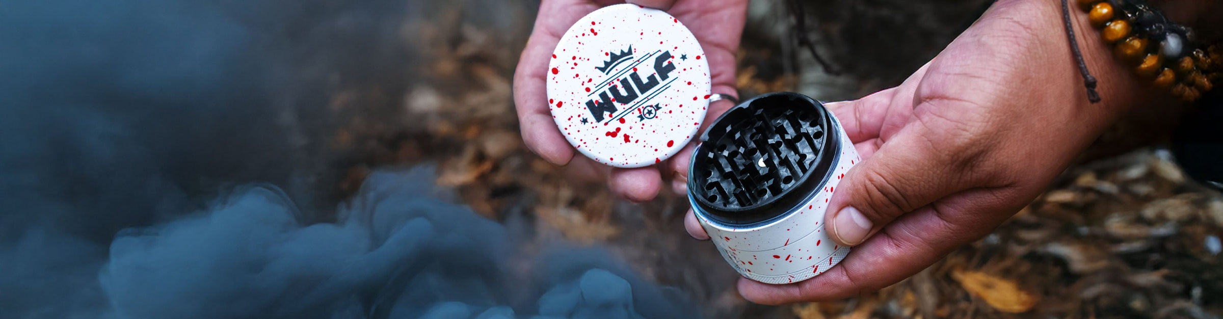 Grinders collection banner with man holding Spatter Grinder above nature trail and dark smoke