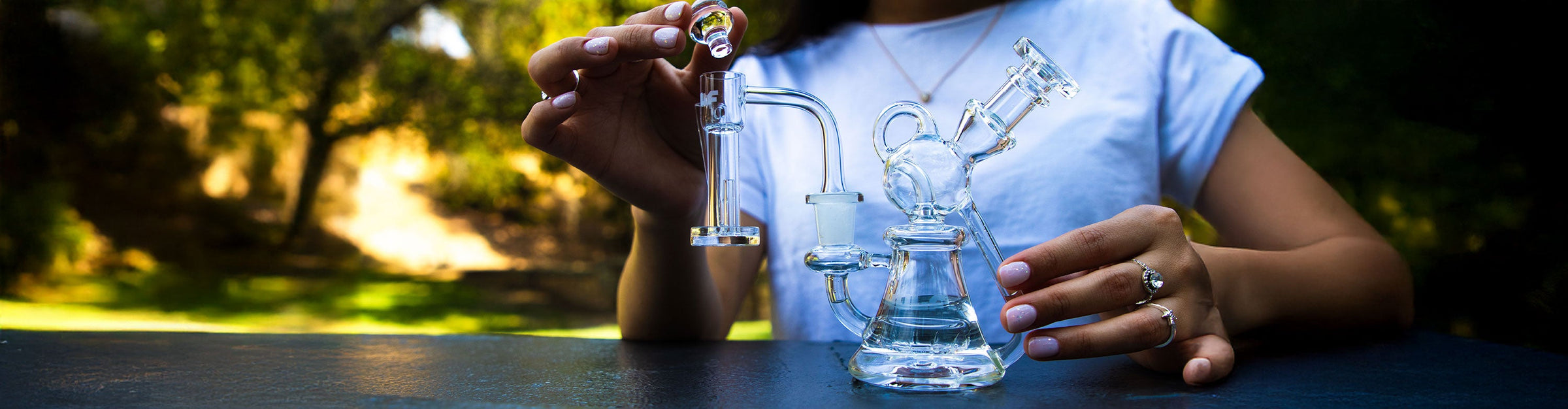 woman holding a carb cap for the Wulf Horn and holding the Wulf Revo Dab Rig at park with trees and grass in background